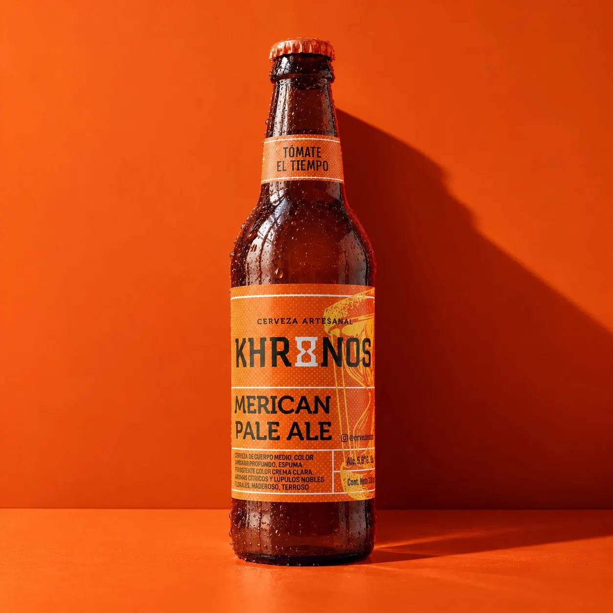 Botella de Cerveza Khronos American Pale Ale con el tagline “Tómate el tiempo” sobre fondo naranja.